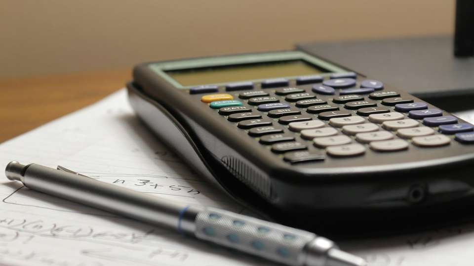 A calculator and a pen on a page of handwritten notes