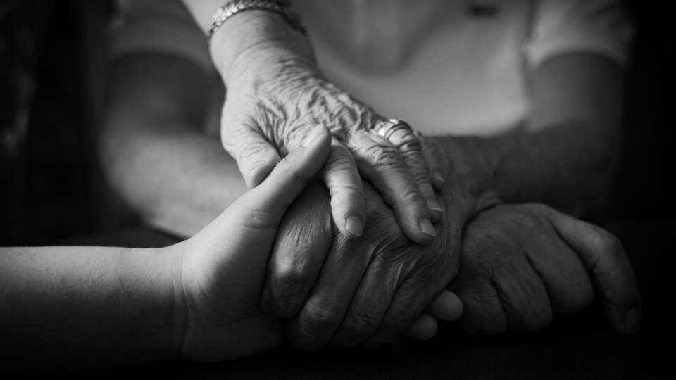 A younger hand holding an older person's hands, in black and white