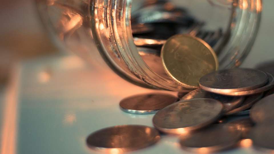 Coins spilling out of a glass jar on a table