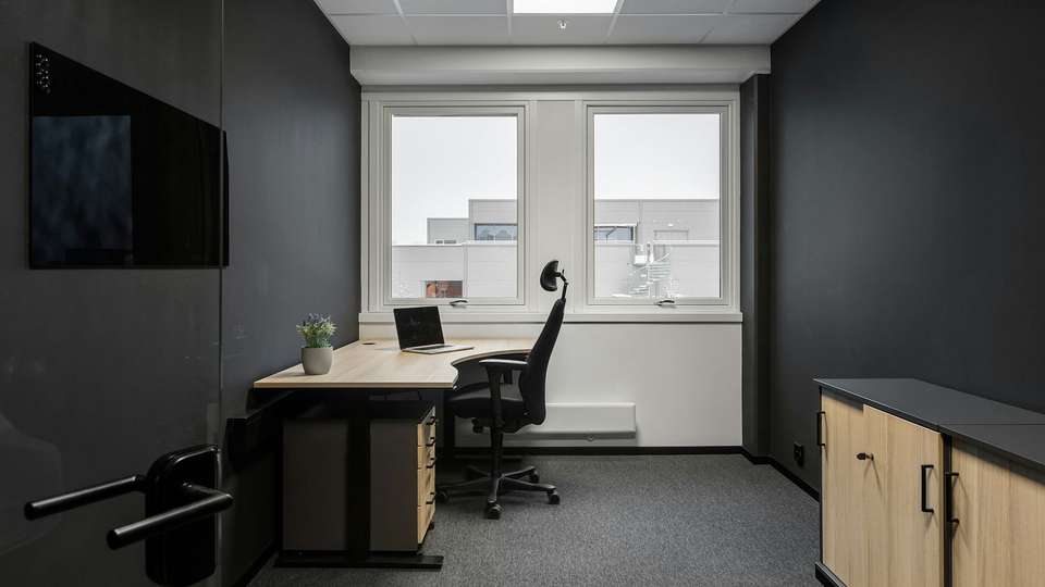 An empty office with a desk, a laptop and an office chair in front of two windows