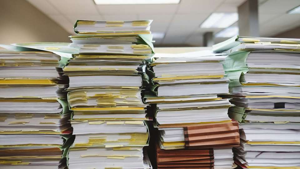 Tall stacks of paper files and folders on a desk in an office
