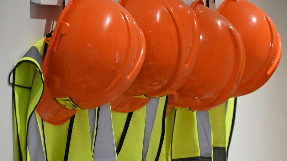 Orange hard hats and reflective safety vests hanging on a wall