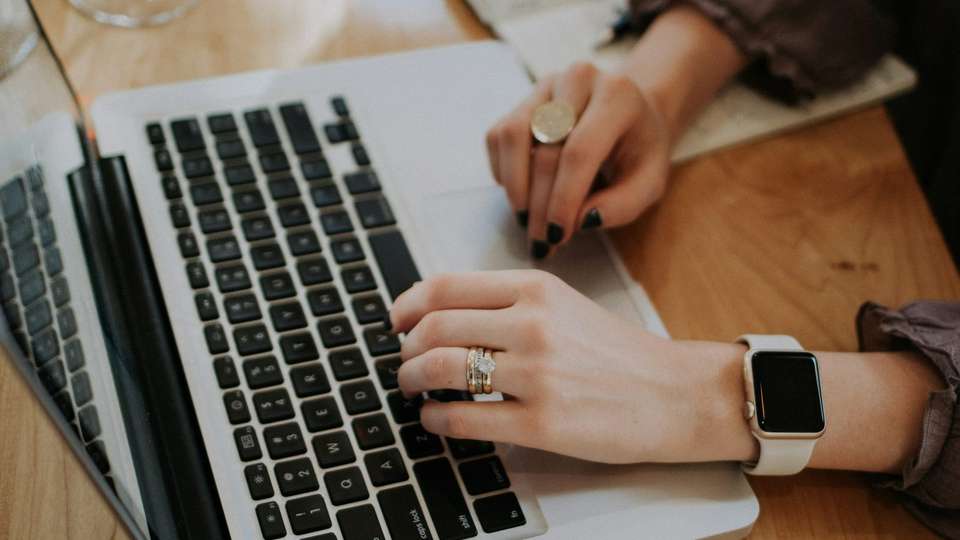 Hands typing on a laptop on a wooden table next to an open notebook