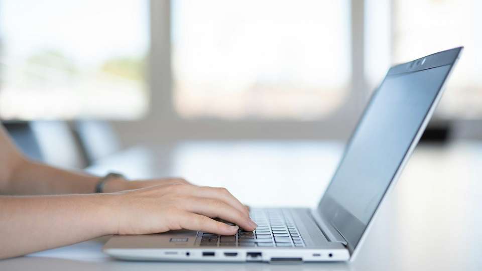 Hands typing on a laptop on a white table by a bright window