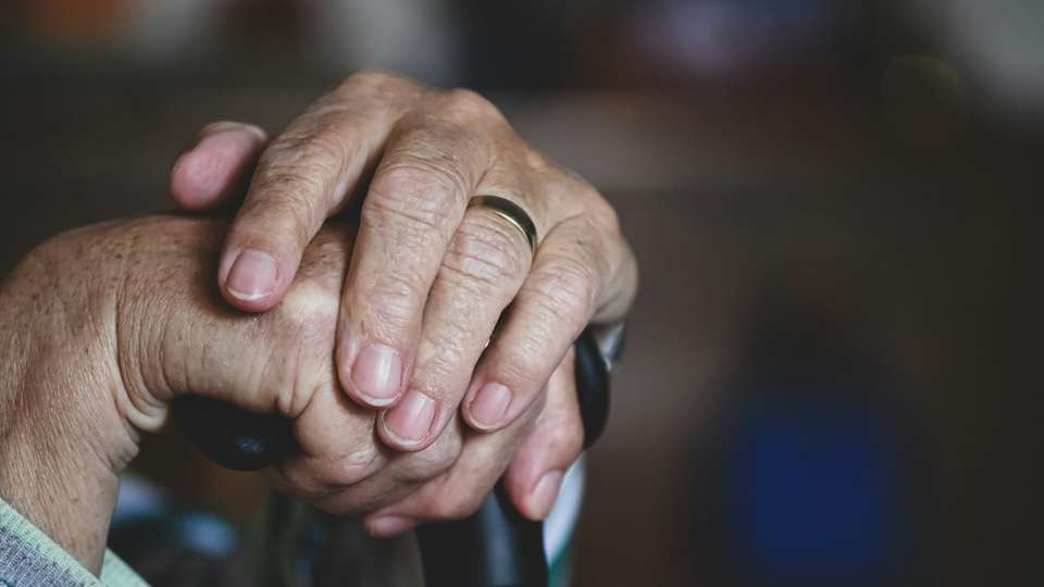 An older person's hands resting on the handle of a walking stick