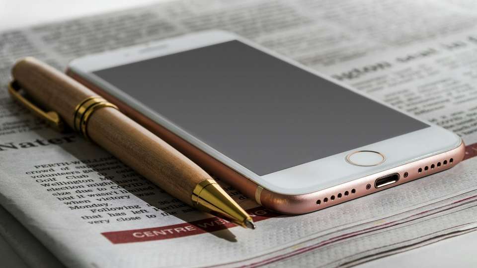 A smartphone and a pen lying on a folded newspaper