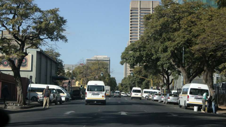 Minibus taxis and cars on a tree-lined street in Pretoria