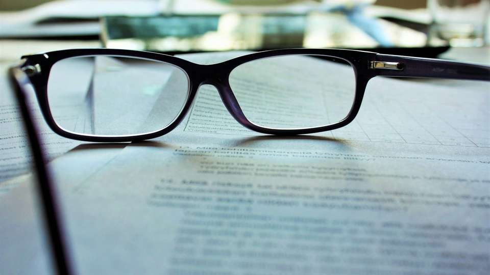 A pair of black-framed reading glasses lying on a printed document