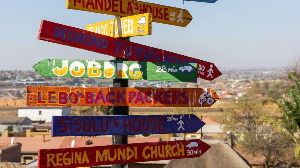 Colourful hand-painted signposts in Soweto pointing to Joburg, Mandela's House, Sisulu's House and Regina Mundi Church