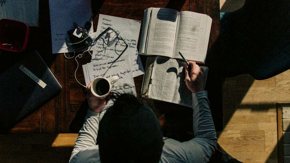 A student studying at a desk with books, notes and a cup of coffee, seen from above