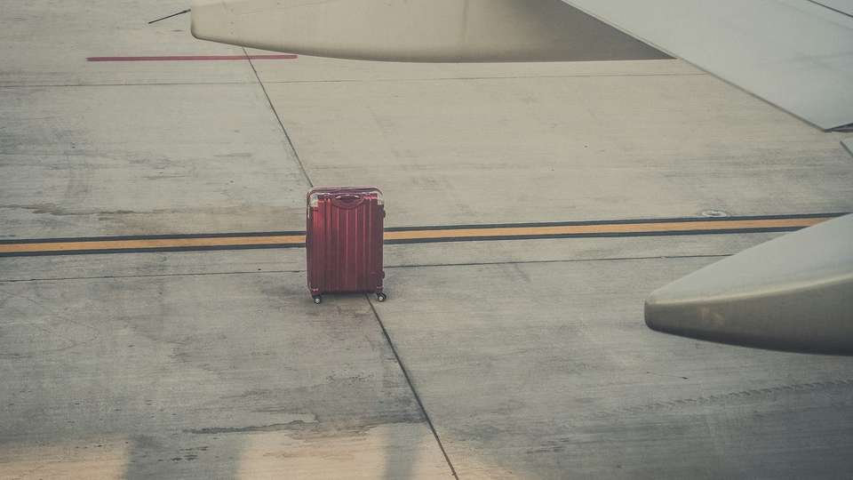 A red suitcase on the tarmac beside an aeroplane wing