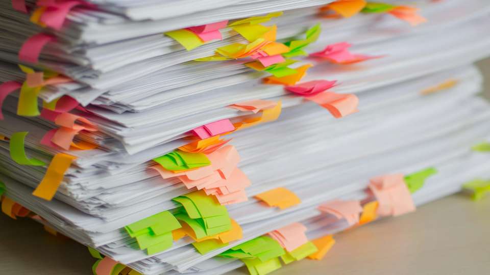 A tall stack of printed papers marked with pink, orange and green sticky tabs