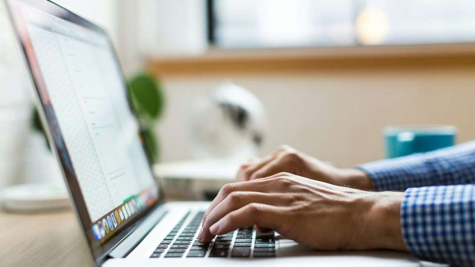 Hands typing on a laptop at a desk near a window