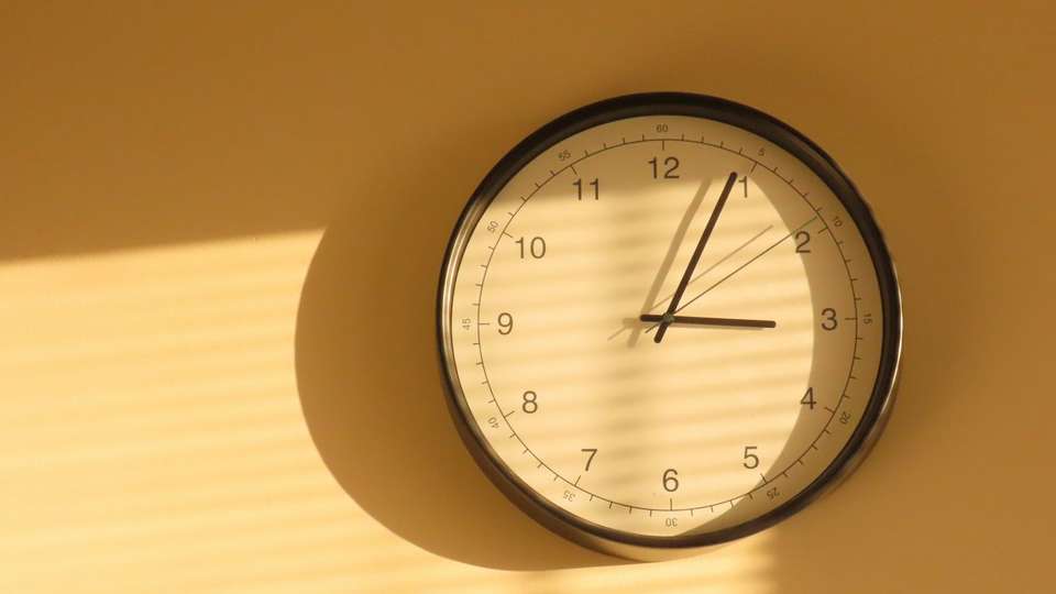 A round wall clock in warm afternoon light, casting a shadow on the wall