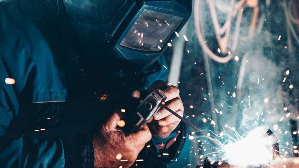 A welder in a protective mask working on metal, with sparks flying