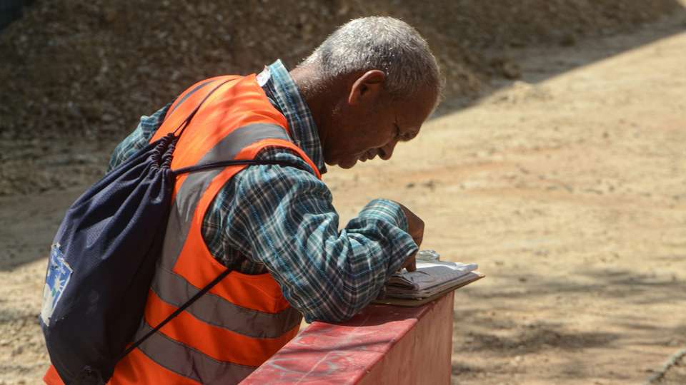 A worker in a reflective vest filling in paperwork on a low wall at a building site
