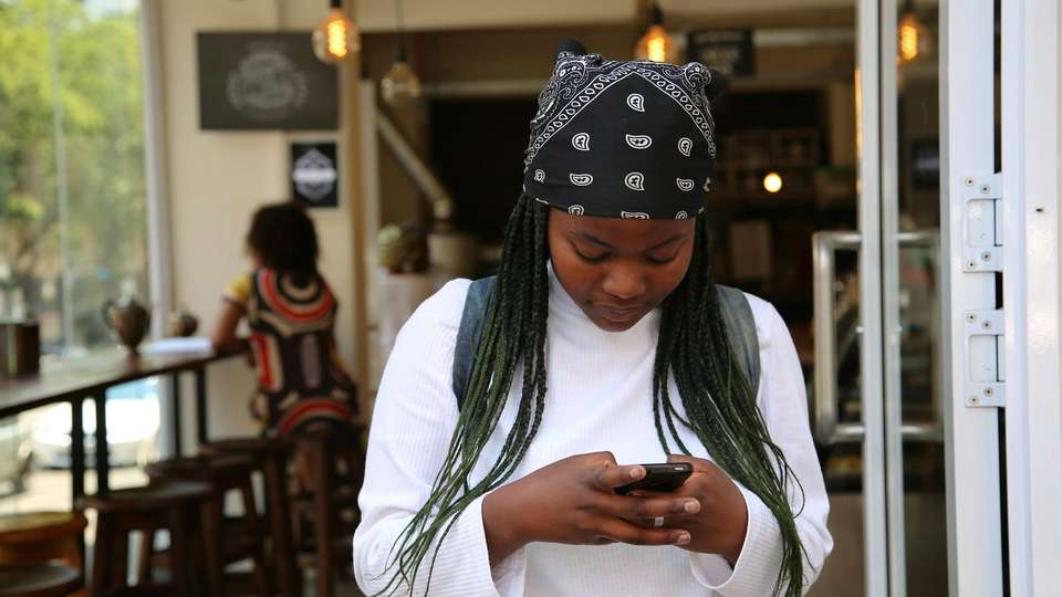 A young woman typing on her phone at the door of a café